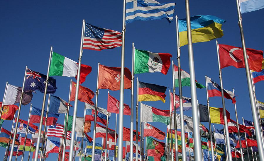 Photo of a grouping of national flags with a blue sky behind them. 