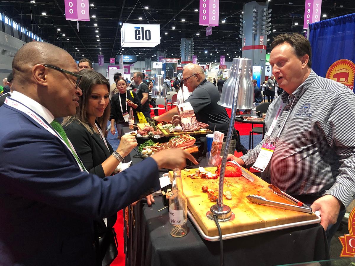 FAS Administrator Daniel Whitley (left) commends the Compart Family Farm’s “bang bang” bacon wrapped sausage and delectable, grilled pork loins from the family’s 55-year-old pork breeding program that takes place on Compart-owned small farms in Minnesota and Iowa.