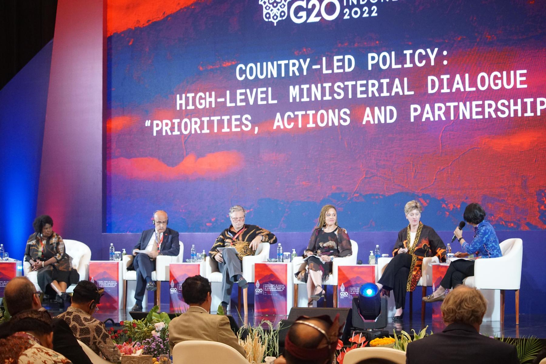 G20 officials seated across stage with red and blue background