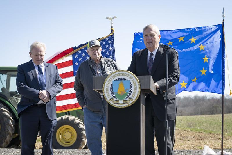 Three met at podium on farm with US and EU flags in background