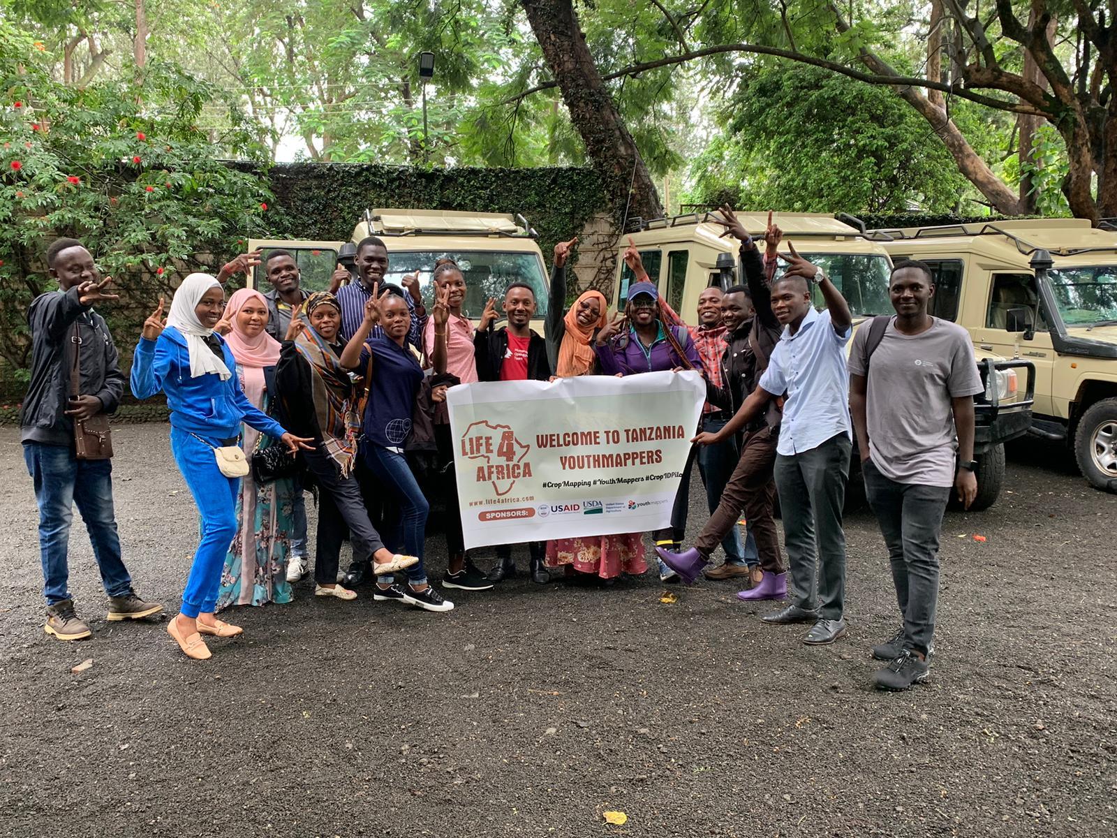 A group of 14 YouthMappers from Tanzania pose in front of jeeps before going out into the field for research.