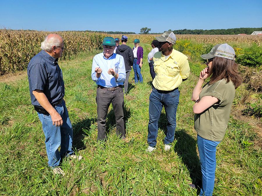 People standing in a half circle in a wheat field on Bobby Hutchison’s farm chatting about the Hutchison family’s work in conservatory farming.