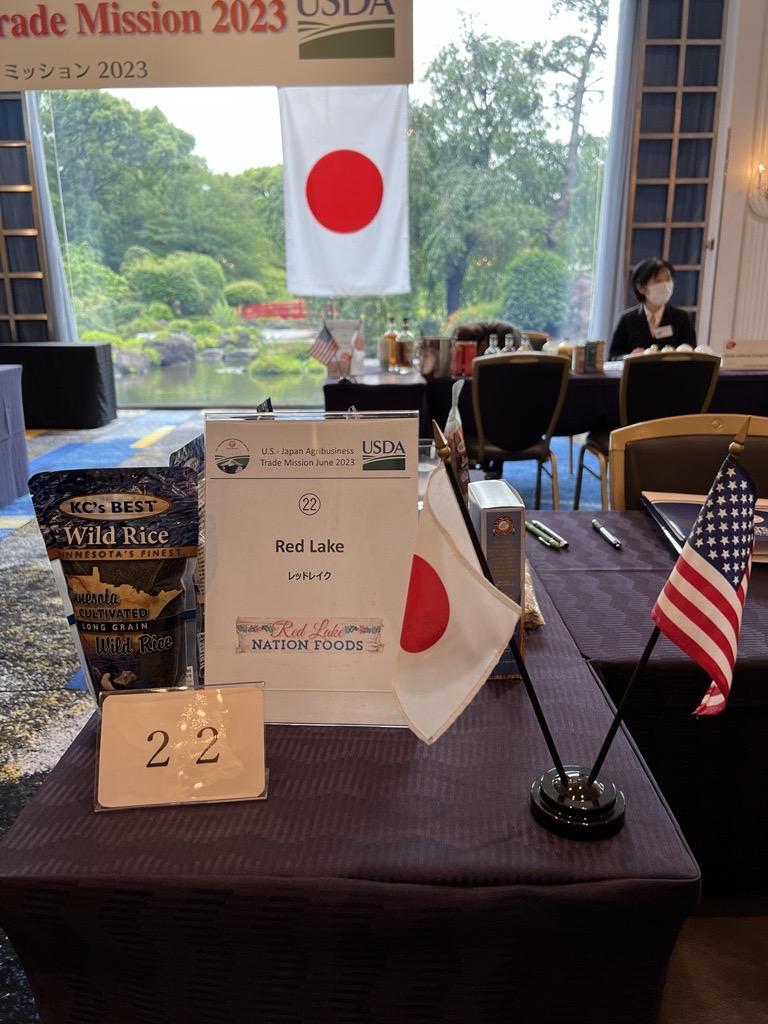 Placard that reads “Red Lake” sits on a table next to table flags of Japan and the United States and a bag of KC’s Best Wild rice. 