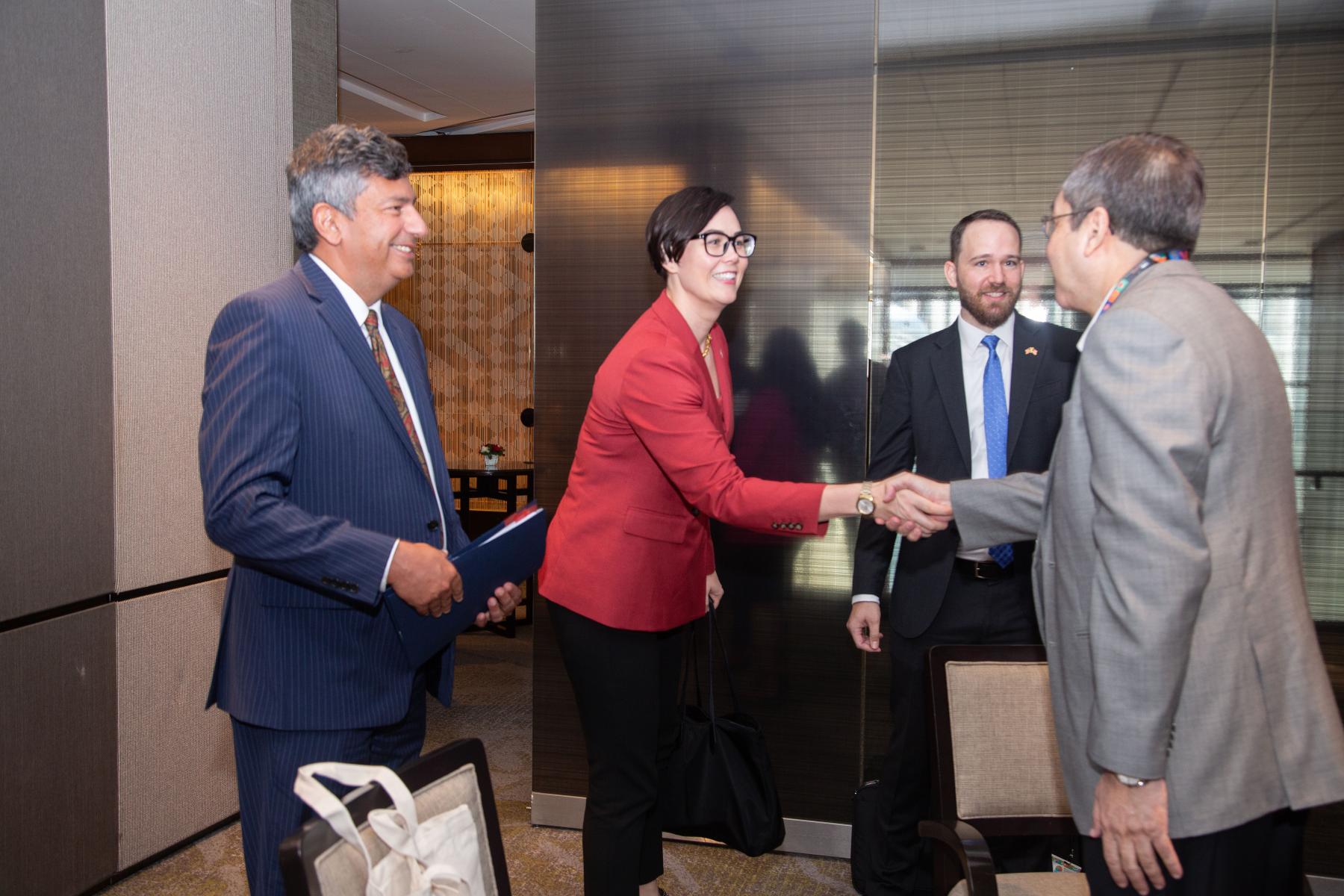 A woman and a man shake hands at the beginning of a meeting with two other people standing in the background.