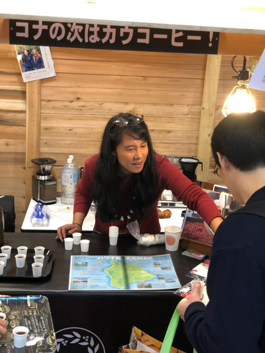 A woman stands at a table with coffee samples and a map of Hawaii.