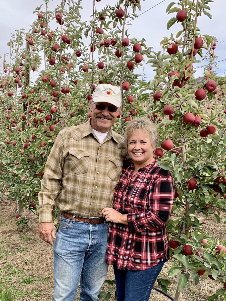 A man and woman stand in front of an apple tree.