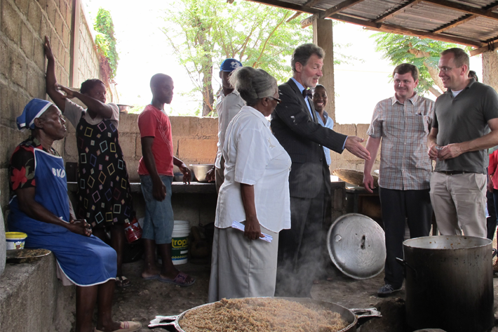 Marie Juslene Pelerin (in white), principal of Haiti’s National School of Ganthier, shows the preparation of a school meal to U.S. Ambassador to Haiti Peter Mulrean (to her right) and FAS Administrator Phil Karsting (far right).