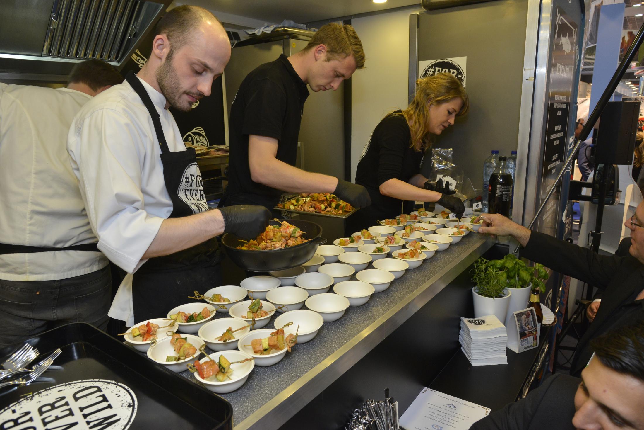 A food truck in the USA Pavilion at Seafood Expo Global attracts a crowd as the chef dishes up fresh, high-end seafood bites and snacks made with Alaskan salmon, cod and scallops.